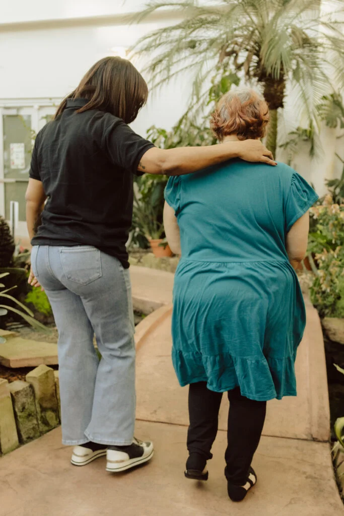 Questions to Ask Before Choosing HCBS or VA Medical Foster Home Support 1 Essential Living Support caregiver and adult client sitting together on a bench during a supportive conversation in a peaceful community environment.