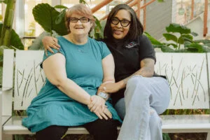 Essential Living Support caregiver sitting beside an adult client during a positive and supportive community interaction.